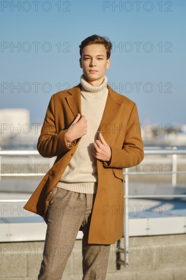 Spring, autumn outfit. Street fashion. Young man in checkered trousers, sweater wraps wool coat