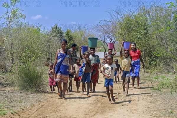 Malagasy women and children with buckets of water on their heads walking from river back to village