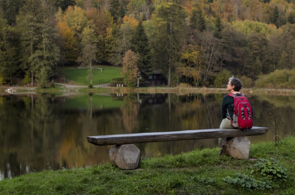 Older woman with backpack, Best Ager, sitting lonely on wooden bench, Ebnisee, Kaisersbach, autumn,