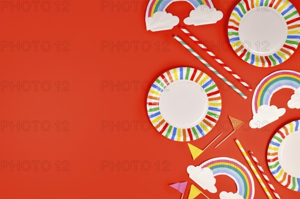 Rainbow themed party flat lay with colorful plates, napkins and drinking straws on red background