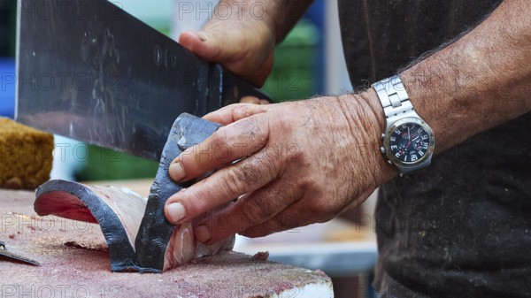 Man cuts tuna into strips with large knife, fish market, old town, Catania, east coast, Sicily,