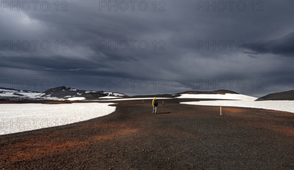 Hikers in snow-covered volcanic landscape with volcanic sand and petrified lava, crater of Askja