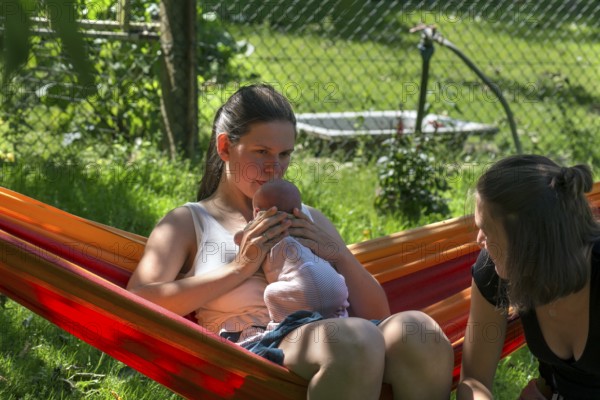Young mother with baby in a hammock in the garden, sister on the right, Mecklenburg-Vorpommern,