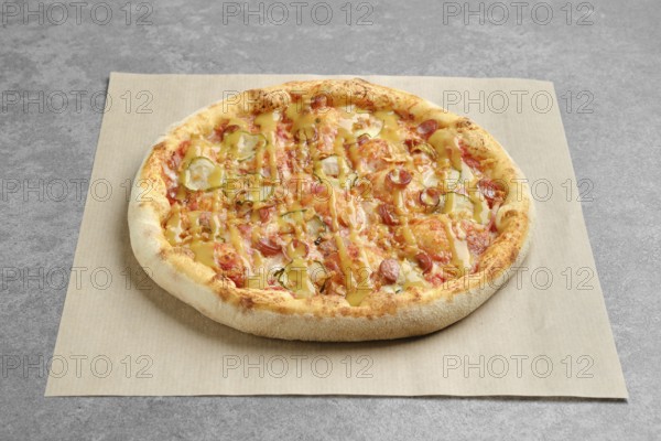 Top view of pizza with thin sausage and pickled cucumber on parchment paper