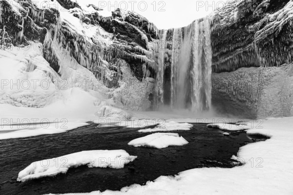 Skogafoss waterfall with icy and snowy rock face, black and white photo, Sudurland, Iceland, Europe