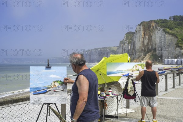 Landscape painters painting fishing boats, caïques on beach and sea cliffs at seaside resort Yport,