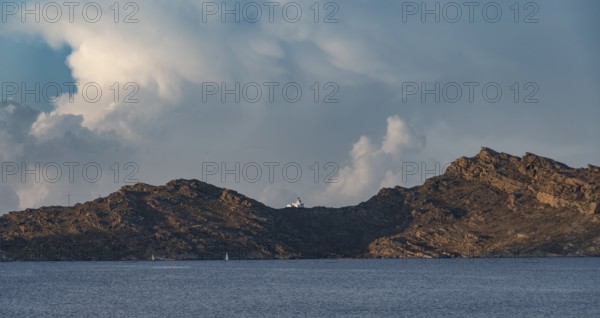 Rocky coast with lighthouse Akrotiri Korakas with blue sea, dramatic cloudy sky Paros, Cyclades