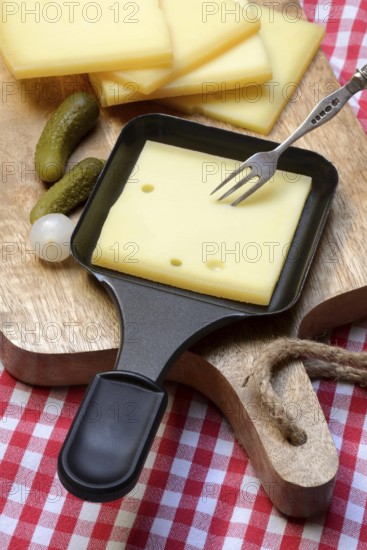 Raclette, cheese slices on wooden board and in raclette pans, Switzerland, Europe