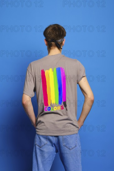Back view of young man in t-shirt with lgbtq flag on blue background