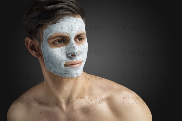 Portrait of a beautiful, relaxed young man with a face mask made of clay, skin care for face and