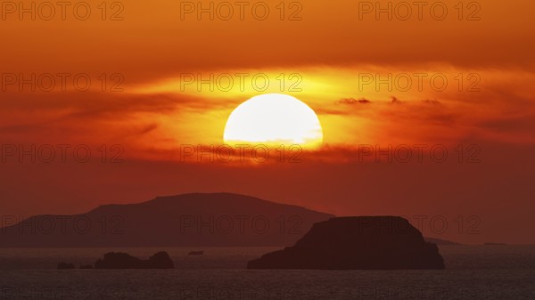 Sun setting over the sea with islands on the horizon, sky in intense orange tones, sunset, Kassos,
