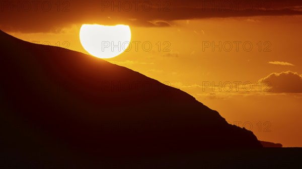 Sinking sun behind a mountain slope, intense orange light in the sky, sunset, Kassos, Karpathos,