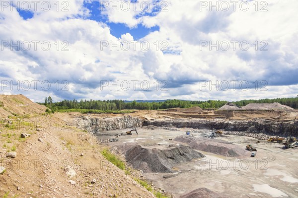 Active quarry with piles of gravel and machinery in a forest landscape in summer, Sweden, Europe