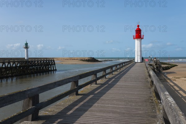 Red and green lighthouses along a wooden walkway on the coast under a blue sky, green lighthouse in