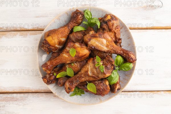Smoked chicken legs with herbs and spices on a ceramic plate on a white wooden background. Top