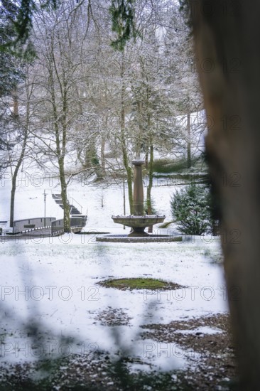 Snow-covered park landscape with a central fountain and surrounding trees, spa garden, Bad Wildbad,
