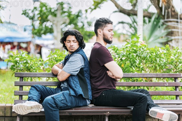 Two angry friends sitting on a park bench. Two friends arguing on a park bench