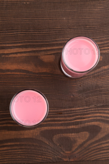 Sweet strawberry liqueur in glass on a brown wooden background. top view, close up, flat lay
