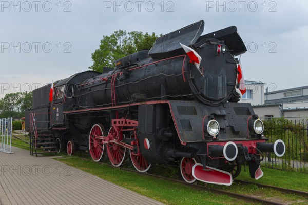 Front view of a black steam locomotive with red details in an open-air museum, Polish steam