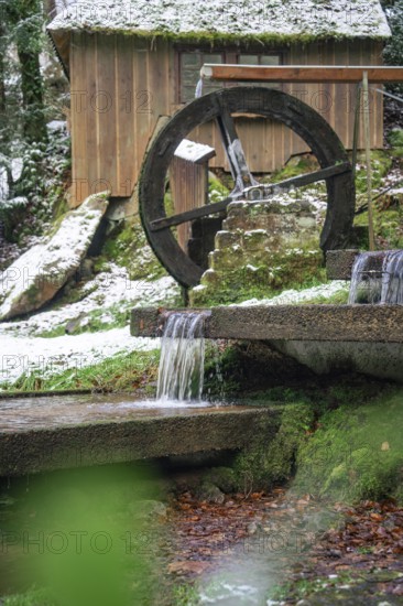 An old water wheel turns next to a hut with snow and running water, spa garden, Bad Wildbad, Black
