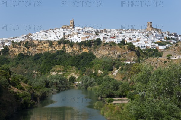 Whitewashed houses on a green hill along a river under a clear sky, Arcos de la Frontera, Guadalete