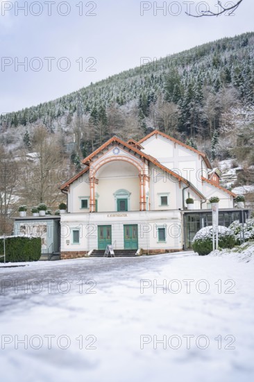 A snow-covered theatre building against a wooded mountain backdrop in winter, Königliches