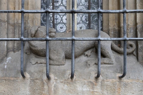 Dog sculpture behind the iron grating of a pointed arch window at the late Gothic hall church of St