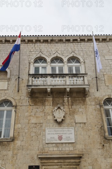 Old beige and tan stone cladded Trogir Town Hall building facade with balcony, flags, arched