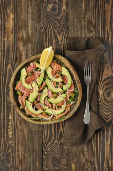 Overhead view of salad with fresh salmon, avocado and onion served in a wooden bowl on a rustic