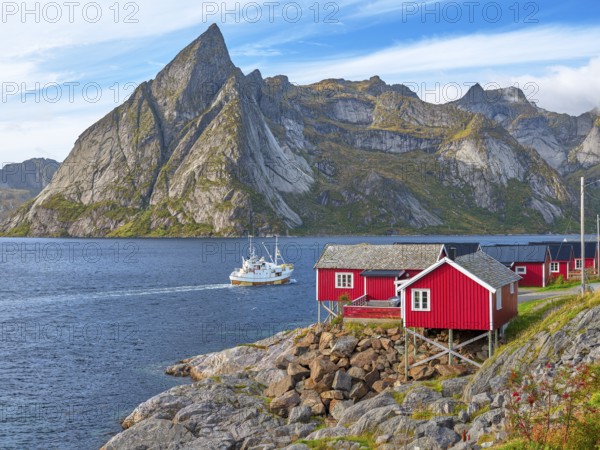 Rorbuer in Hamnoy, fishing boat in front of the mountain Olstinden, blue sky, Moskenesoya, Lofoten,