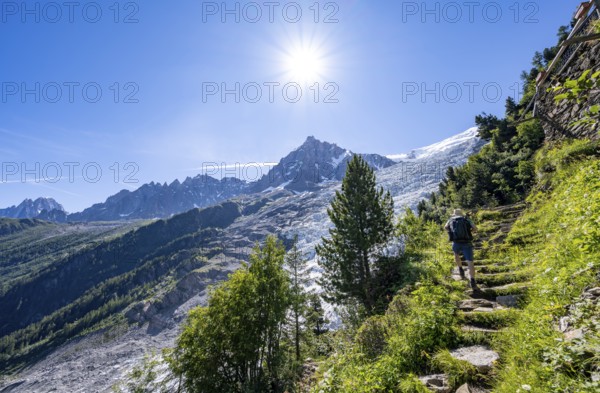 Hiker on hiking trail La Jonction, view of glacier Glacier des Bossons with sun star, behind summit