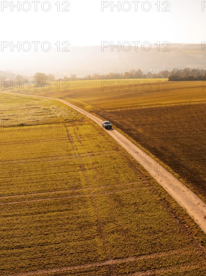 A car on a long dirt road, surrounded by vast golden fields in autumnal scenery, electric car VW