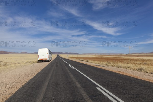 A bus on a deserted country road through a wide, dry landscape under a blue sky, national road B4