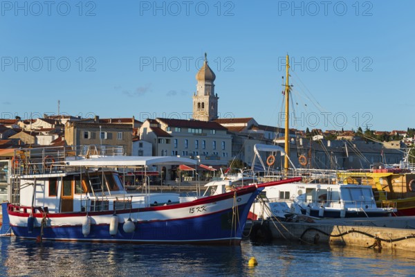A harbour full of boats and ships with a striking bell tower in the background under a sunny sky,