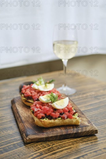 A wooden serving board holds two generous portions of bruschetta topped with diced salmon and egg