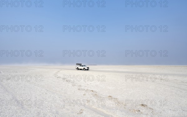 Four-wheel drive Toyota Hilux with roof tent, driving over salt pan, lone car in large wide plain,