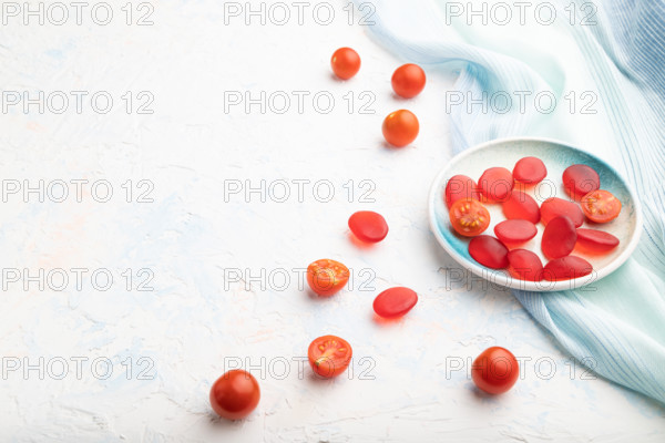 Jelly tomato candies on white concrete background and blue linen textile. copy space, side view