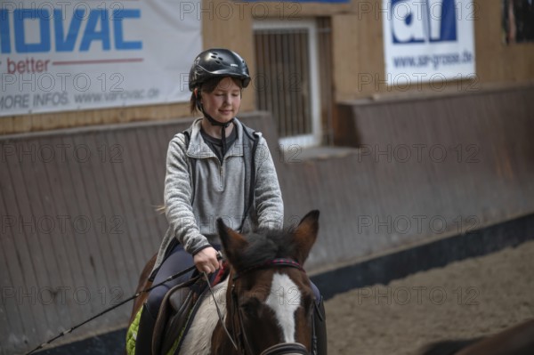 Little girl, 10 years old, in the saddle on a horse in an indoor riding arena,