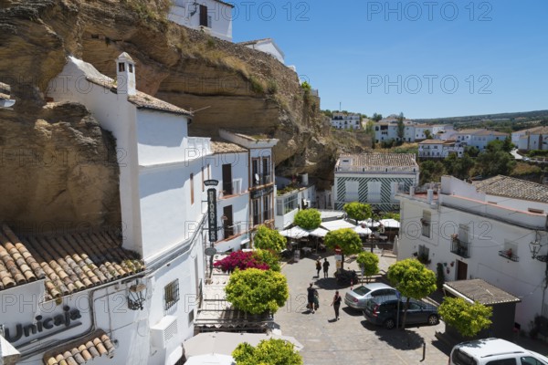 Square with cars and cafés in Setenil de las Bodegas under rocks with white houses, blue sky, cave