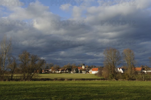 Vast landscape with a small village under a dramatic cloudy sky, surrounded by green meadows and