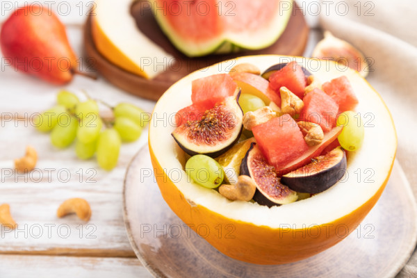 Vegetarian fruit salad of watermelon, grapes, figs, pear, orange, cashew on white wooden background