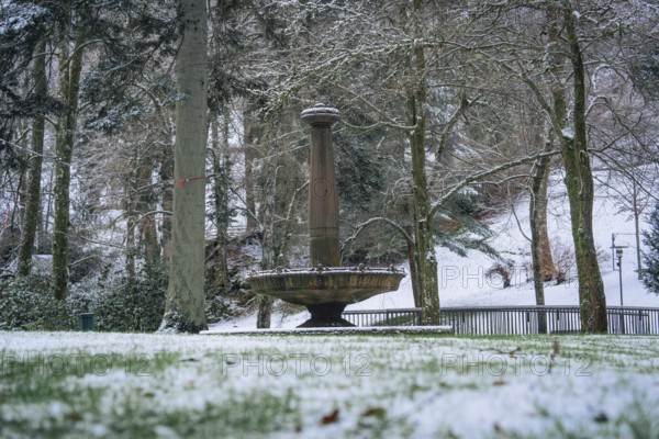 A snow-covered fountain under tall trees in the winter park, spa garden, Bad Wildbad, Black Forest,