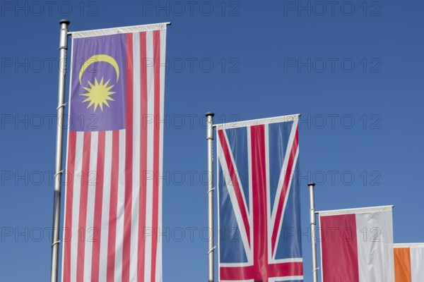 Several flags of different countries fly side by side under a clear blue sky, Malaysian flag,