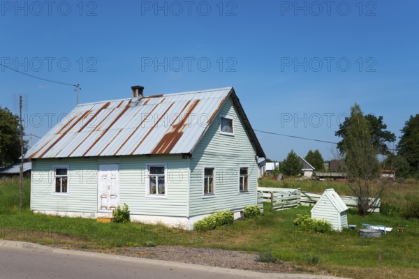 Small green wooden house with metal shingle roof and garden in a quiet rural setting, house and dog