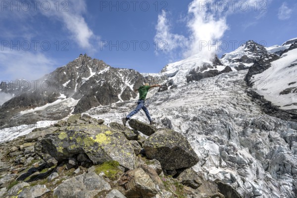 Mountaineer jumping from rock to rock, high alpine glaciated mountain landscape, La Jonction,