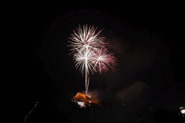 Large fireworks display glows colourfully in the night sky above an illuminated building, New