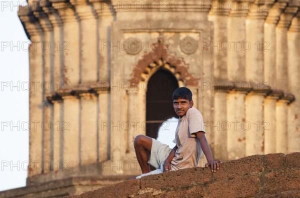 Young man on wall in front of terracotta temple, Bishnupur, Bankura district, West Bengal, India,