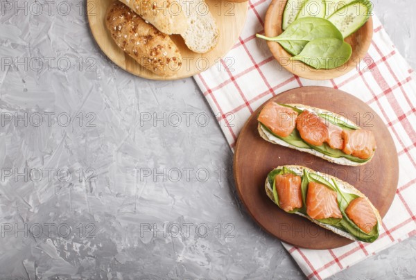 Smoked salmon sandwiches with cucumber and spinach on wooden board on a gray concrete background.