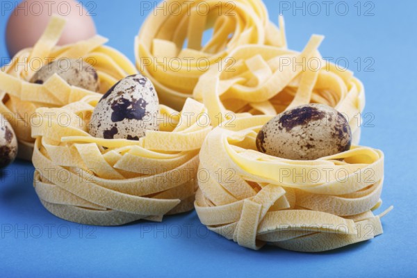 Raw uncooked tagliatelle pasta with quail eggs on a blue pastel background. side view, close up