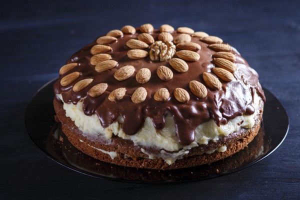 Homemade chocolate cake with milk cream and almonds on black wooden background. close up